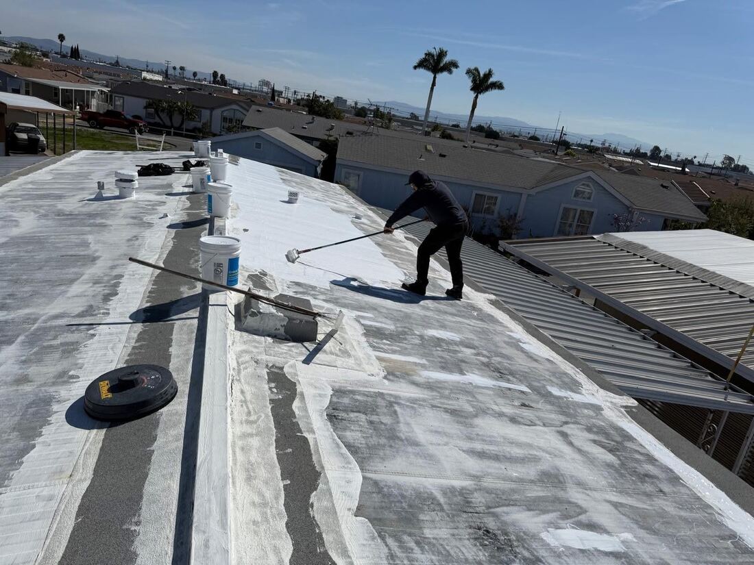Roofing crew applying white elastomeric roof coating to a flat roof